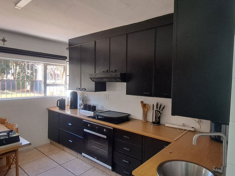 Functional kitchen featuring dark cabinetry, built-in oven and hob, tiled flooring, and a window with security bars overlooking the exterior.