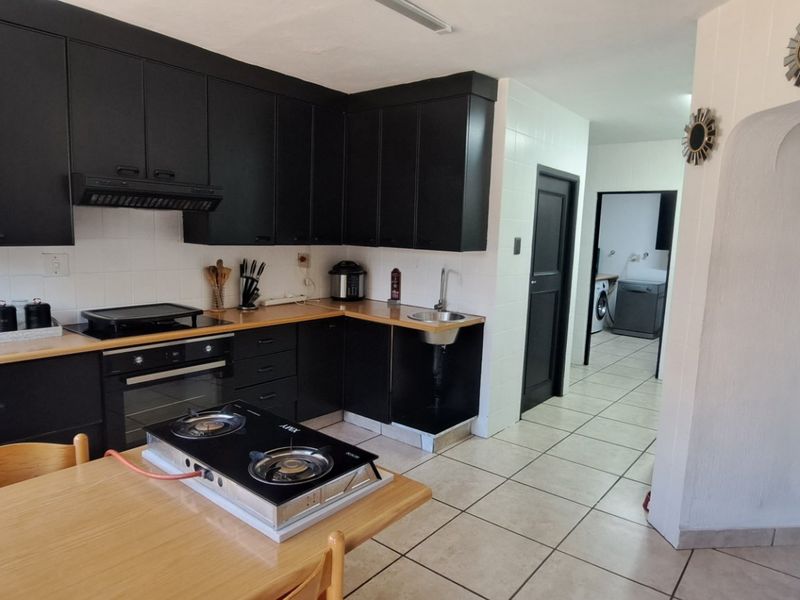 Kitchen featuring black cabinetry, tiled flooring, and a built-in oven, with an adjacent utility area visible through the doorway.