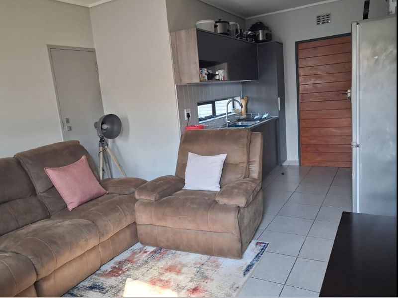 Open plan living area featuring tiled flooring and a compact kitchen corner with built-in cabinetry and sink.