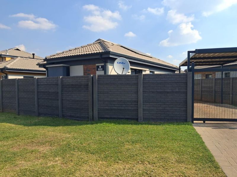 Front view of a modern house featuring a dark brick-style precast boundary wall, paved driveway, metal gate, and a tiled roof with solar panels.