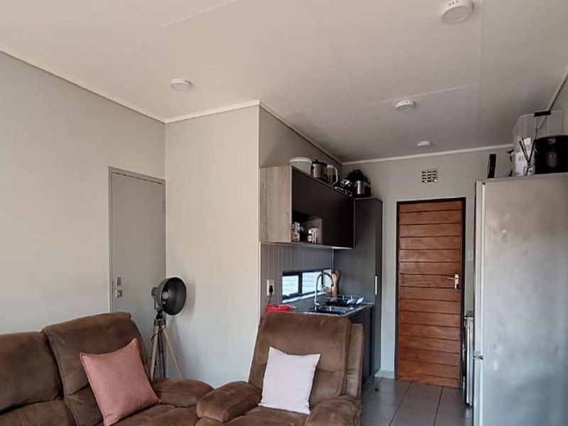 Open plan living area featuring a modern kitchen corner, tiled flooring, and an exposed brick feature wall, creating a functional and contemporary living space.