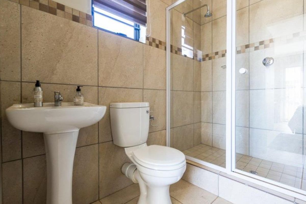 A functional bathroom featuring a pedestal basin, toilet, and a glass-enclosed shower with neutral wall and floor tiling.