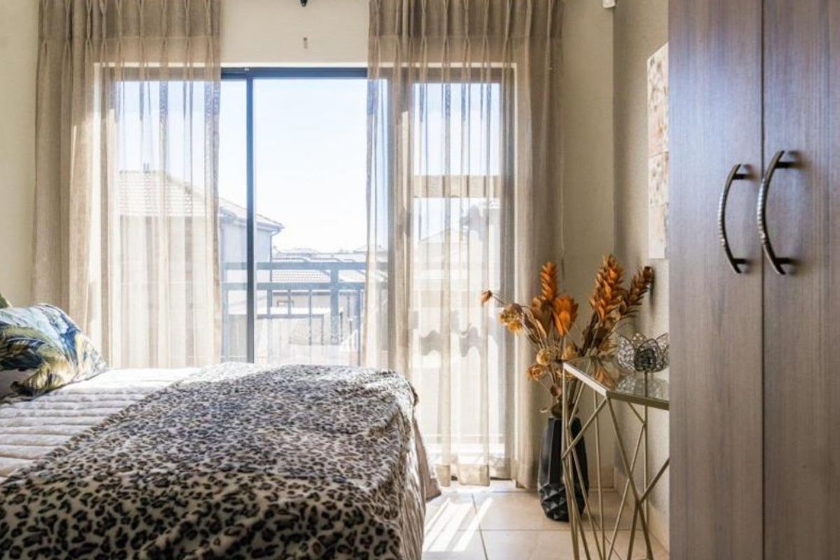 A well-lit bedroom featuring tiled flooring, a built-in wardrobe, and a sliding glass door providing access to an outdoor balcony area.