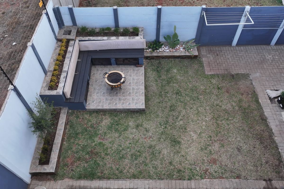 A well-maintained rear garden featuring a paved patio area with built-in seating, raised garden beds, and secure perimeter walling with electric fencing.