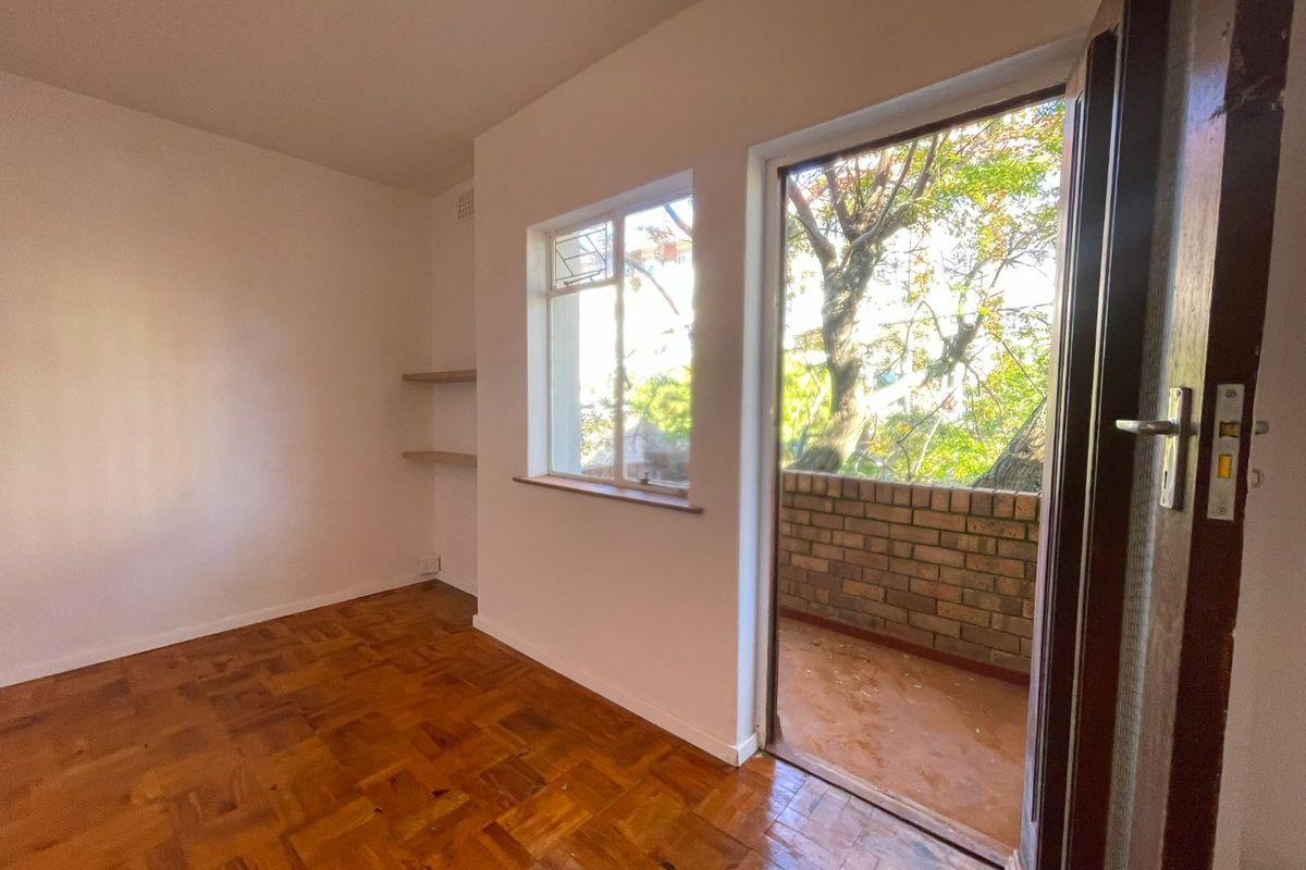 An empty bedroom featuring original parquet flooring, built-in shelving, and direct access to a private balcony.
