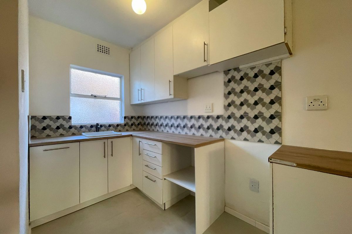 A compact kitchen featuring white built-in cabinetry, wood-look laminate countertops, and a decorative patterned tiled backsplash.