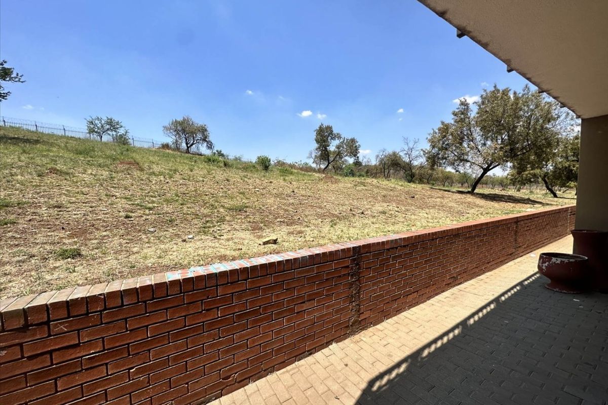 A paved patio area featuring a low brick retaining wall overlooking an open grassy slope and natural landscape.