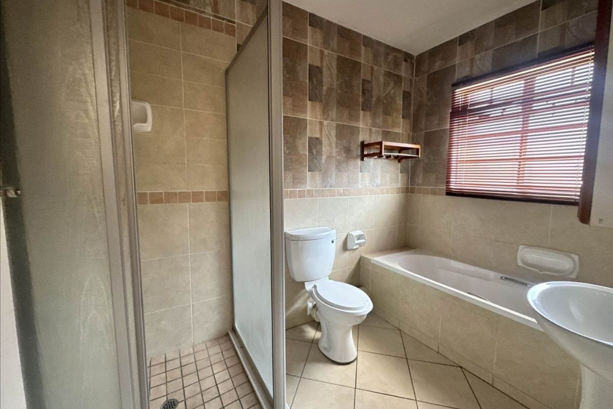 A functional bathroom featuring a separate shower enclosure, bathtub, pedestal basin, and toilet with neutral tiled finishes.