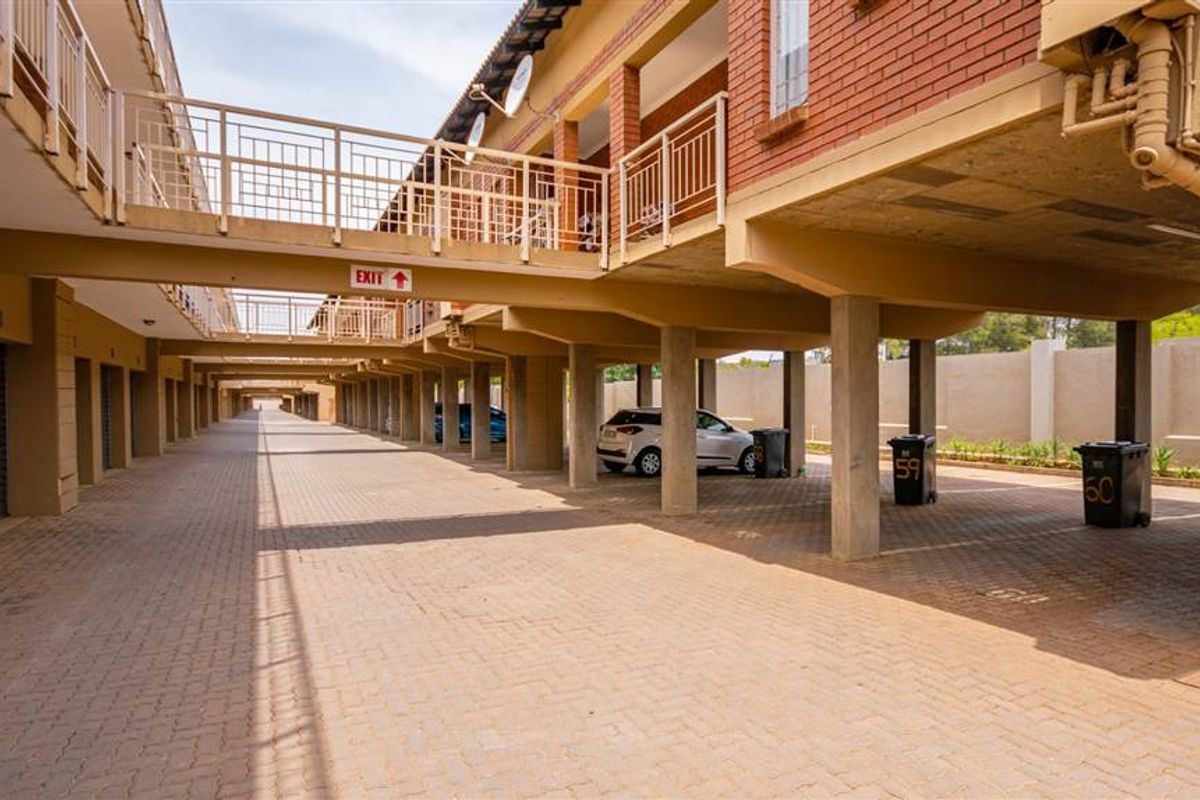 A covered parking area featuring paved ground, concrete support pillars, and metal railings, providing sheltered parking spaces for the apartment complex.