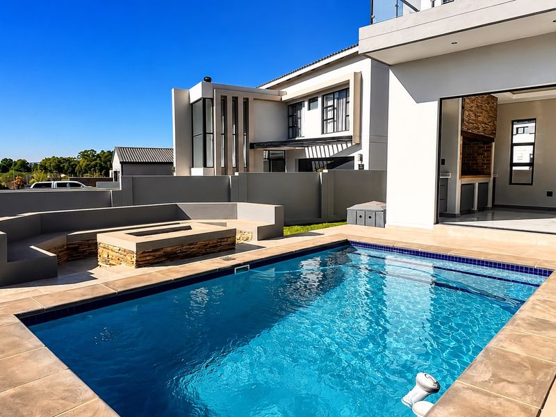 Modern outdoor entertainment area featuring a swimming pool, built-in fire pit with seating, and a covered patio with a built-in braai.