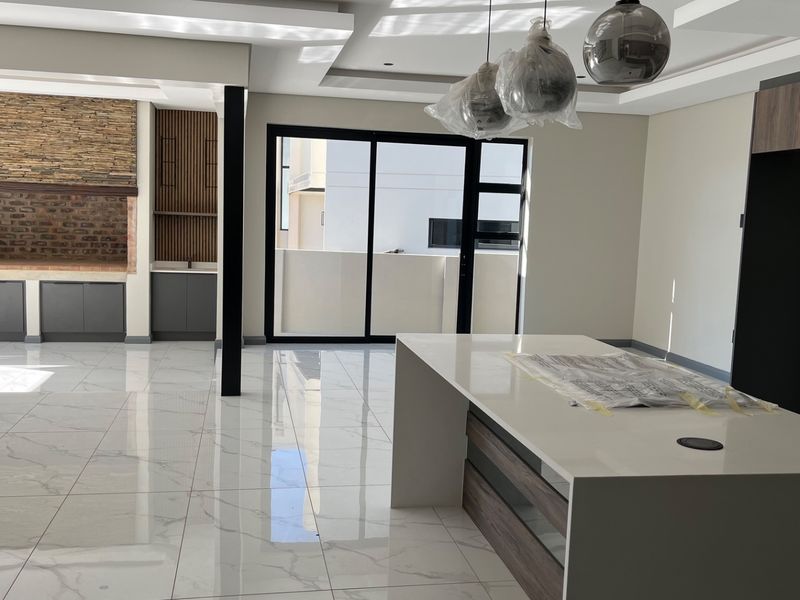 Modern open-plan living area featuring a large kitchen island, stone feature wall with fireplace, and sleek porcelain flooring with access to outdoor space.
