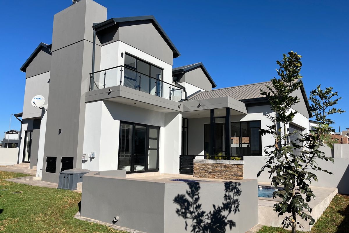 Modern double-story rear elevation featuring a swimming pool, stone-clad accents, a balcony with glass balustrades, and contemporary architectural finishes.