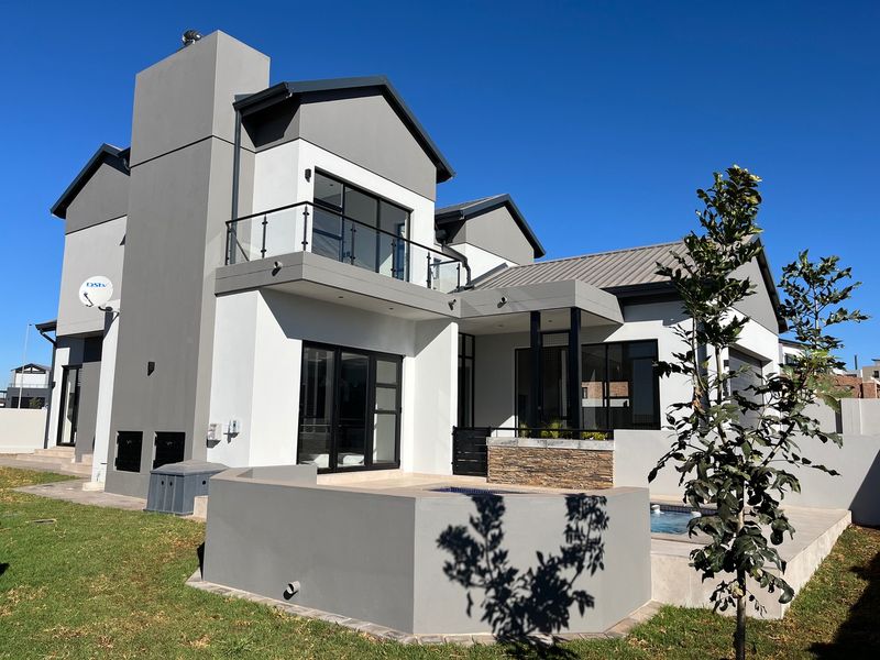 Modern double-story rear elevation featuring a swimming pool, stone-clad accents, a balcony with glass balustrades, and contemporary architectural finishes.