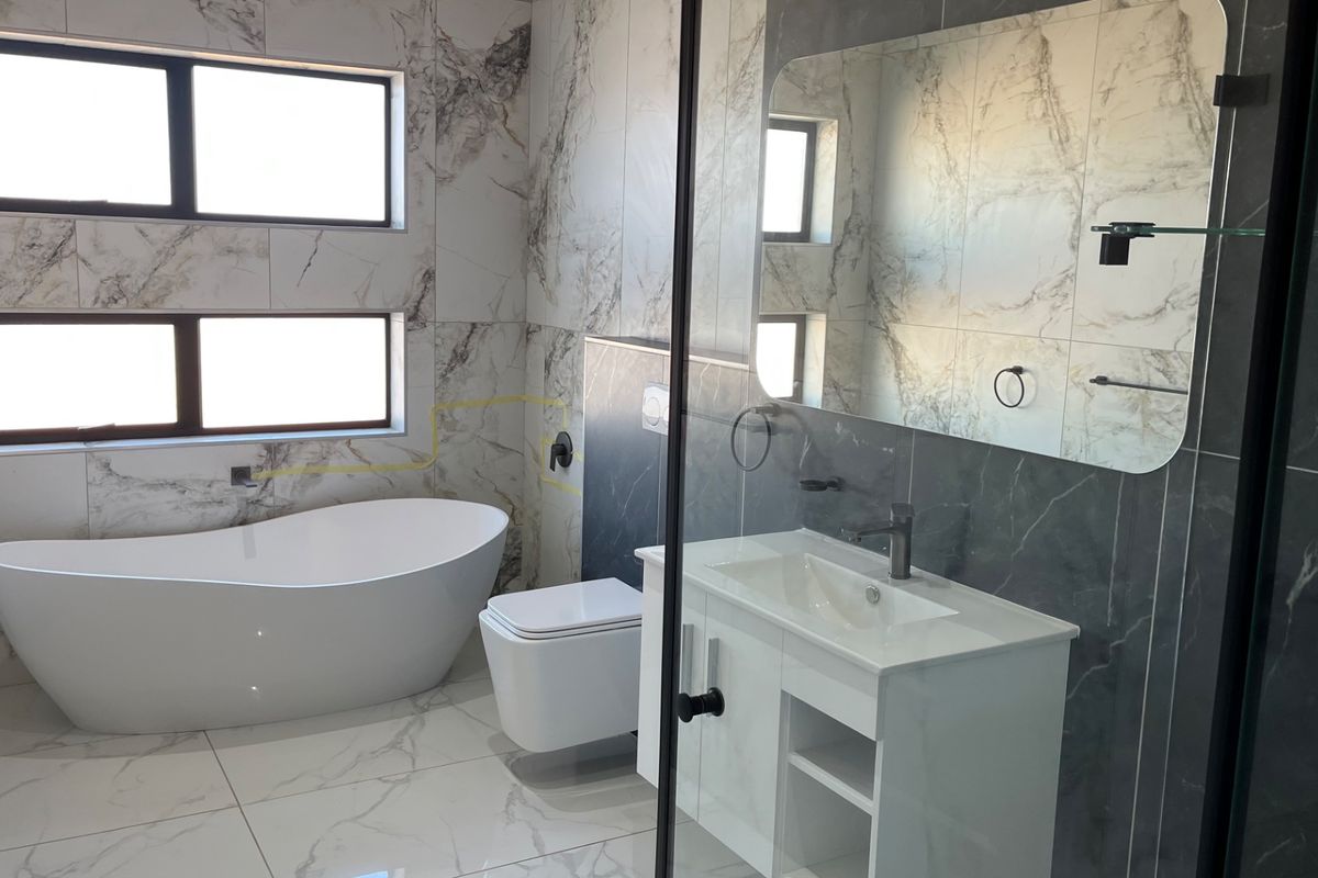 Modern bathroom featuring a freestanding bathtub, wall-mounted toilet, vanity with integrated basin, and a glass-enclosed shower with marble-effect tiling.