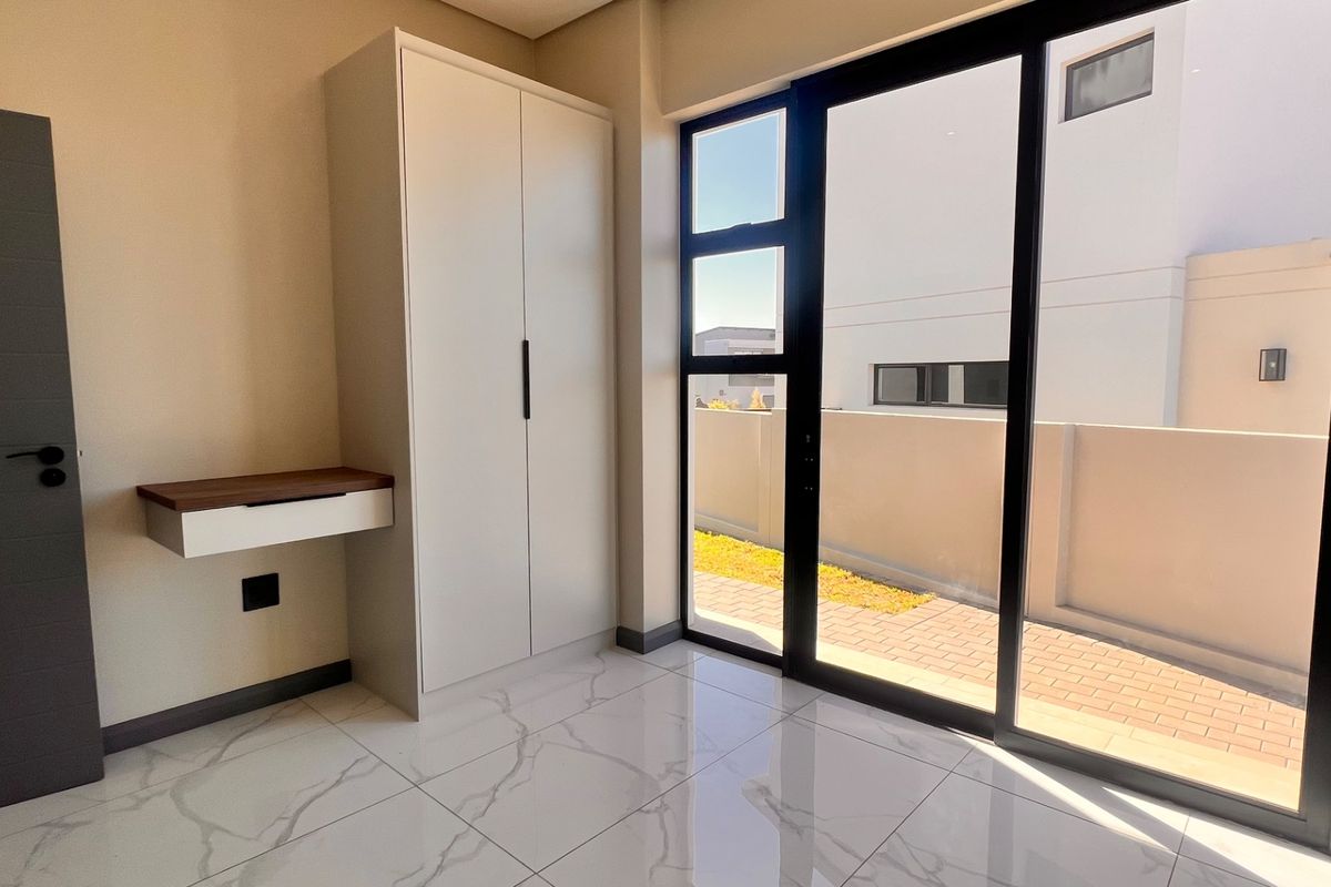 Modern bedroom featuring marble-look floor tiles, a built-in wardrobe, a floating desk, and large sliding glass doors leading to an outdoor area.