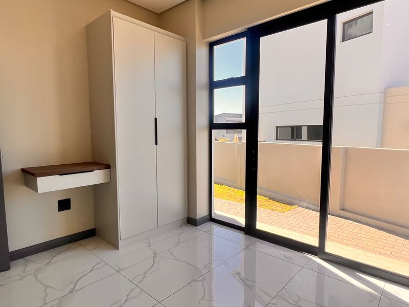 Modern bedroom featuring marble-look floor tiles, a built-in wardrobe, a floating desk, and large sliding glass doors leading to an outdoor area.