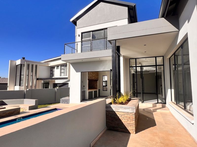 Modern rear exterior featuring a swimming pool, tiled patio area, built-in braai, and a balcony with glass balustrades.