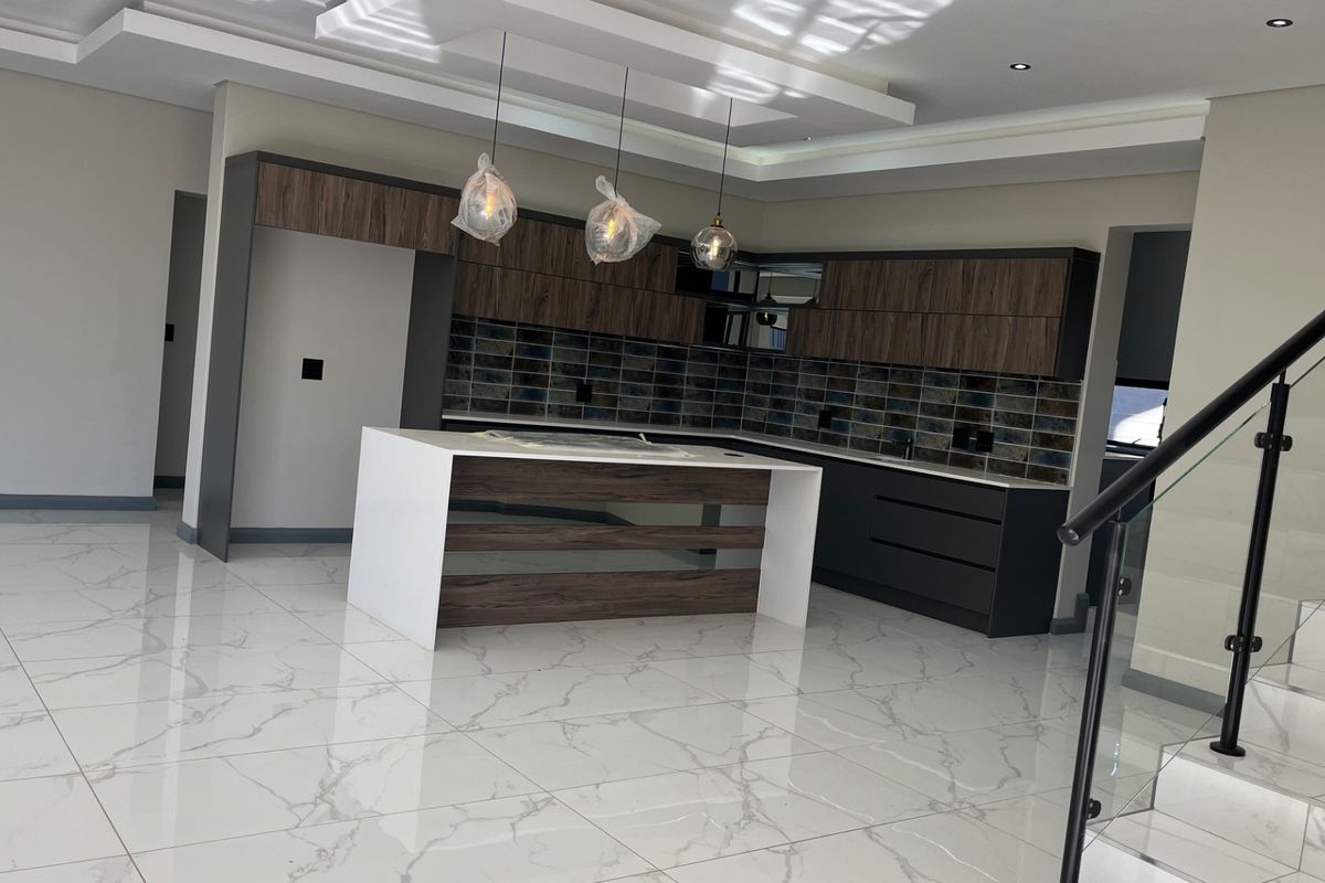 Modern open-plan kitchen featuring a central island, dark wood-grain cabinetry, tiled backsplash, and high-gloss marble-look flooring, adjacent to a glass-railed staircase.