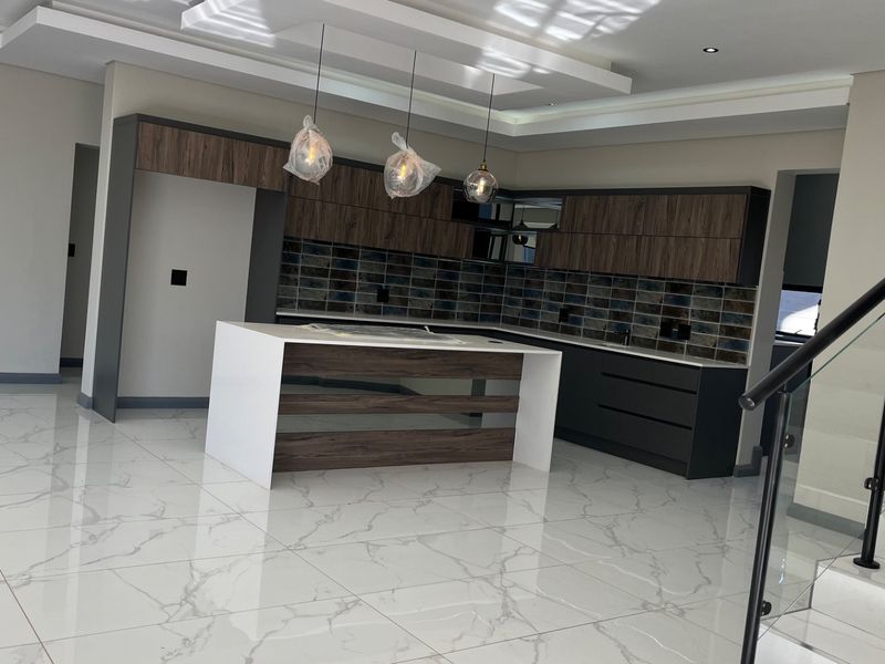 Modern open-plan kitchen featuring a central island, dark wood-grain cabinetry, tiled backsplash, and high-gloss marble-look flooring, adjacent to a glass-railed staircase.