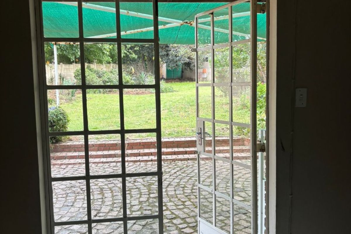 An interior view looking out through open french doors onto a cobblestone patio and garden area.