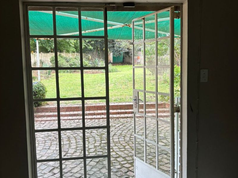 An interior view looking out through open french doors onto a cobblestone patio and garden area.