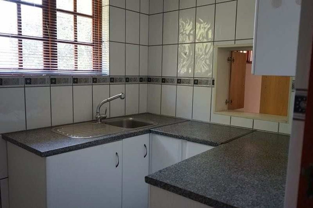 A functional kitchen area featuring laminate countertops, a stainless steel sink, and tiled splashbacks with built-in cabinetry.
