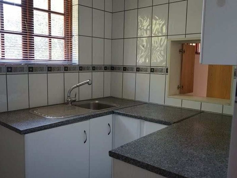 A functional kitchen area featuring laminate countertops, a stainless steel sink, and tiled splashbacks with built-in cabinetry.