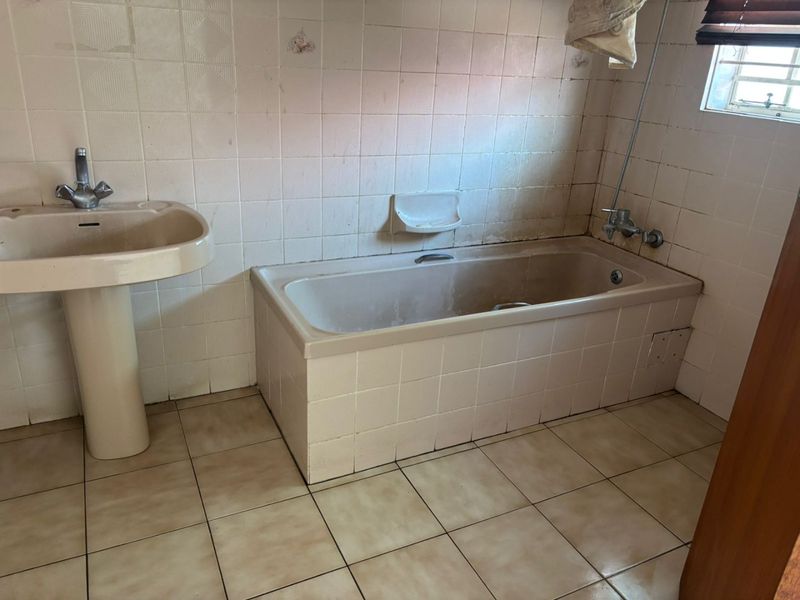 A dated bathroom featuring a pedestal basin and a built-in bathtub with tiled finishes, requiring renovation to update the fixtures and surfaces.