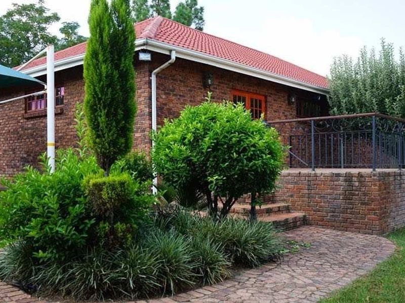 Rear view of a face brick house featuring a raised patio with wrought iron railings, brick paving, and established garden landscaping.