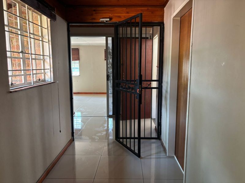 A functional hallway featuring tiled flooring, timber ceiling accents, and a security gate leading to an adjacent living space.