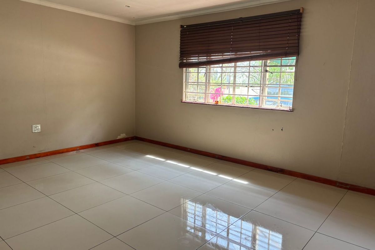 A vacant bedroom featuring neutral wall tones, large floor tiles, timber skirting, and a window fitted with security bars and venetian blinds.