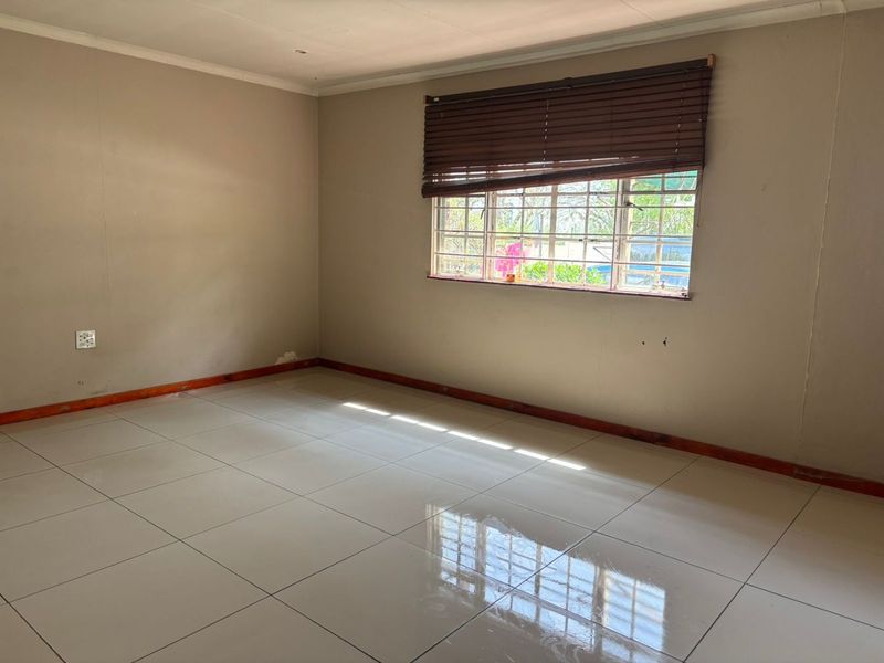 A vacant bedroom featuring neutral wall tones, large floor tiles, timber skirting, and a window fitted with security bars and venetian blinds.