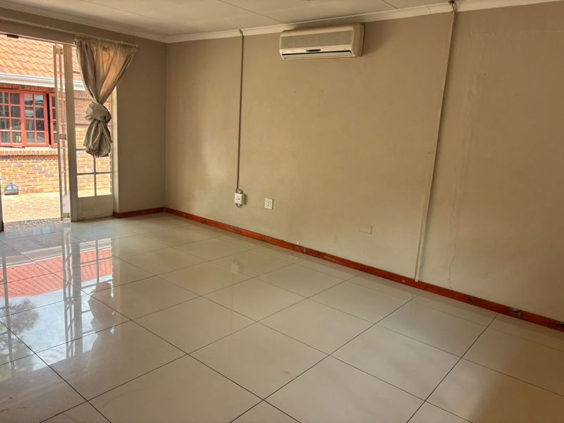 An empty living room featuring tiled flooring, a wall-mounted air conditioning unit, and a glass sliding door providing access to the exterior.