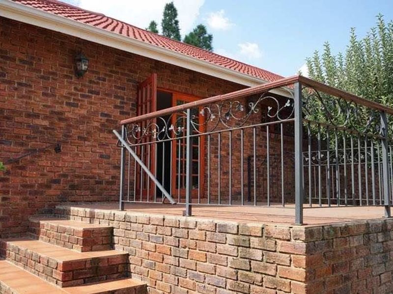 A raised brick patio featuring decorative wrought iron railings, tiled steps, and access to the home via classic wooden french doors.