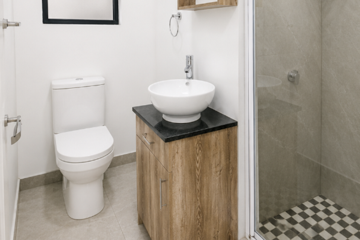 A modern, well-maintained bathroom featuring a vessel sink on a wood-finish vanity, a glass-enclosed shower, and neutral floor tiling.