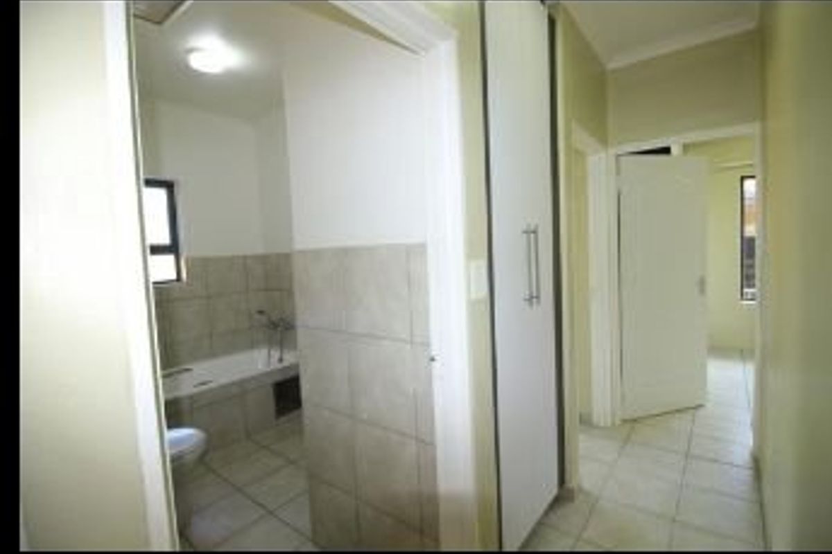 A hallway view showing access to a bathroom with tiled finishes and a built-in cupboard, featuring neutral tones and tiled flooring throughout.