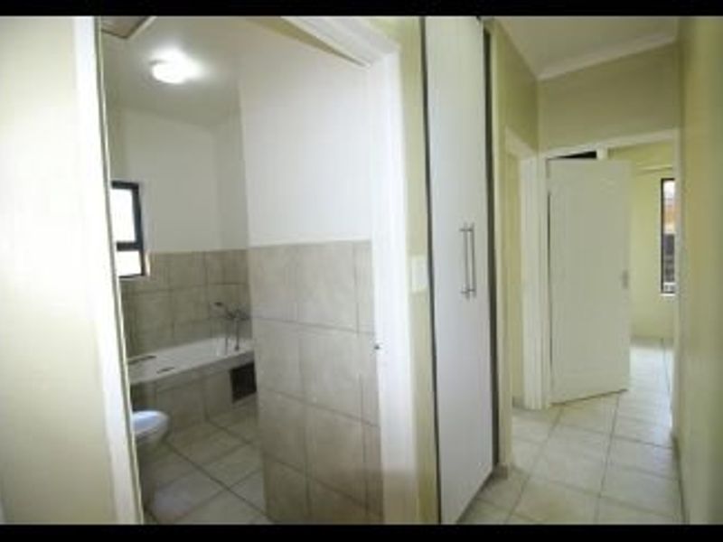 A hallway view showing access to a bathroom with tiled finishes and a built-in cupboard, featuring neutral tones and tiled flooring throughout.