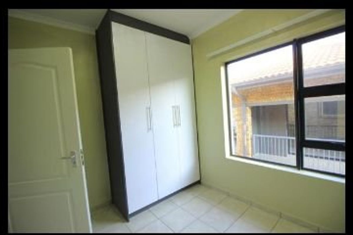 A bright, empty bedroom featuring tiled flooring and a modern built-in wardrobe with white and dark grey finishes.