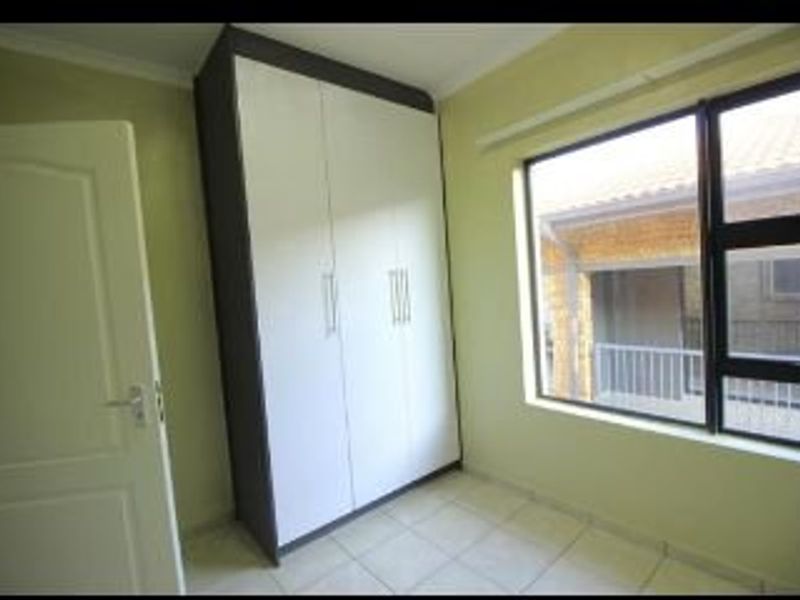 A bright, empty bedroom featuring tiled flooring and a modern built-in wardrobe with white and dark grey finishes.