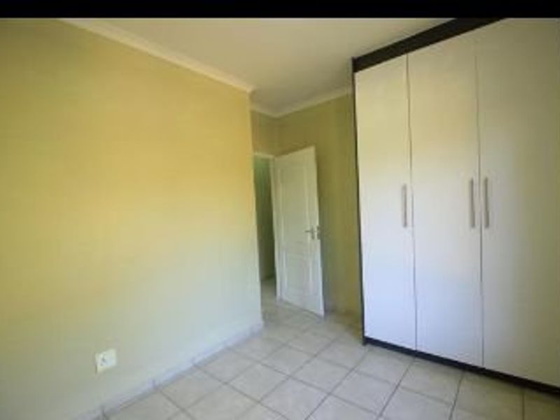 A bright, empty bedroom featuring neutral wall paint, tiled flooring, and modern white built-in cupboards.
