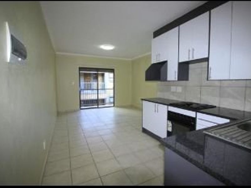 Open-plan kitchen and living area featuring modern cabinetry, granite countertops, built-in appliances, and tiled flooring leading to a balcony.