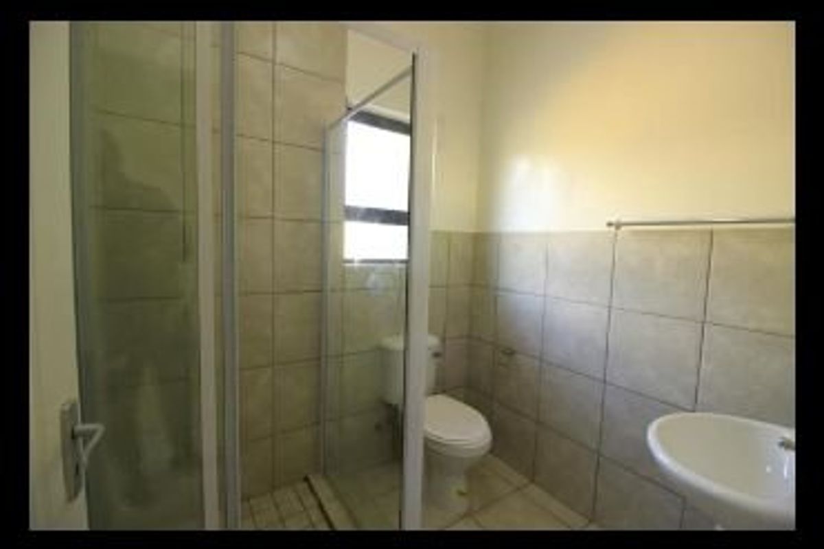 A functional bathroom featuring a glass shower enclosure, pedestal basin, and neutral ceramic wall and floor tiling.