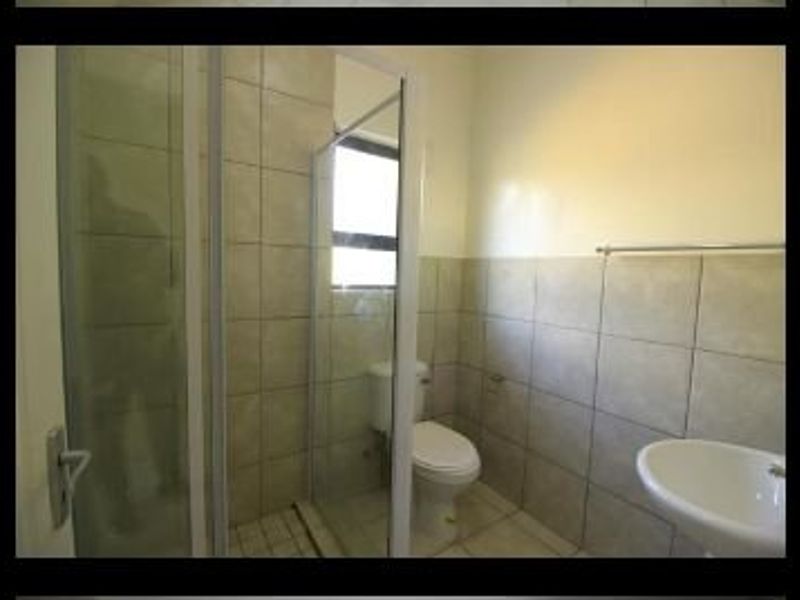 A functional bathroom featuring a glass shower enclosure, pedestal basin, and neutral ceramic wall and floor tiling.