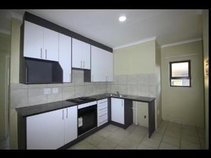 A clean, modern kitchen featuring white and dark cabinetry, granite countertops, built-in oven and hob, tiled backsplash, and neutral tiled flooring.