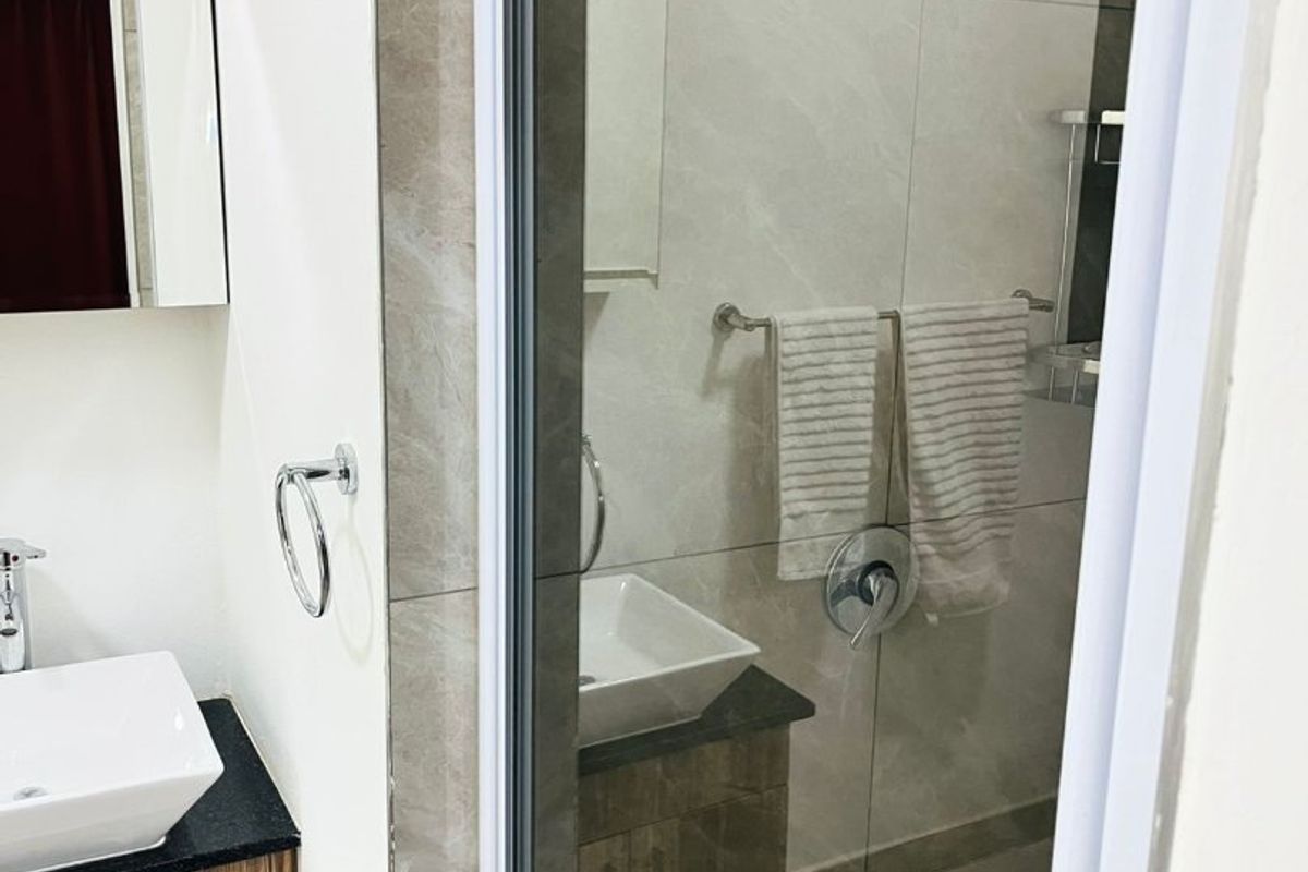Modern bathroom featuring a vessel sink with granite vanity, glass-enclosed shower with rain shower head, and neutral wall and floor tiling.