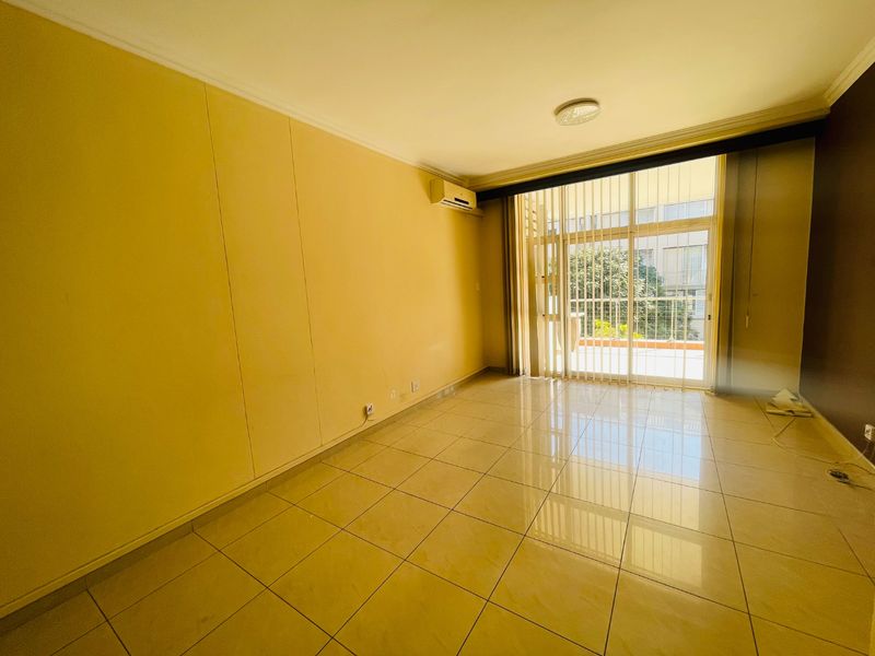 An empty, sunlit living room featuring neutral tiled flooring, an integrated air conditioning unit, and large sliding glass doors leading to a balcony.