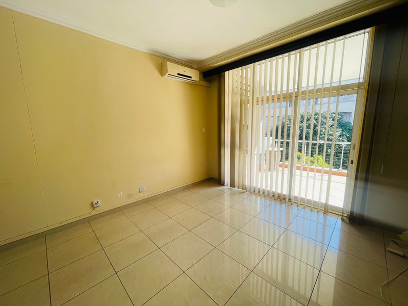 An empty living room featuring tiled flooring, a wall-mounted air conditioning unit, and large sliding glass doors leading to an outdoor balcony.