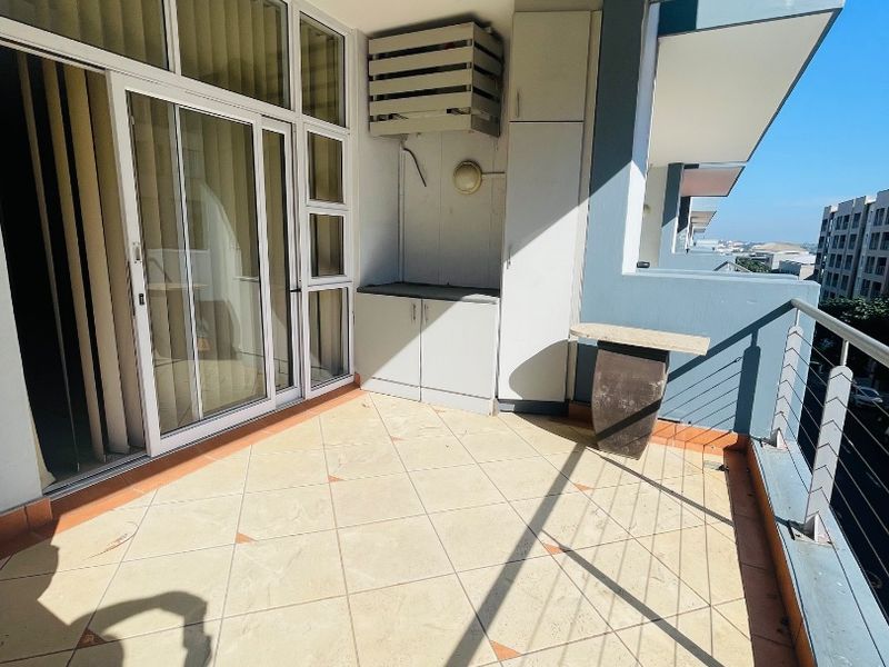 A spacious apartment balcony featuring tiled flooring, built-in storage cabinetry, and a metal balustrade with views of the surrounding urban area.