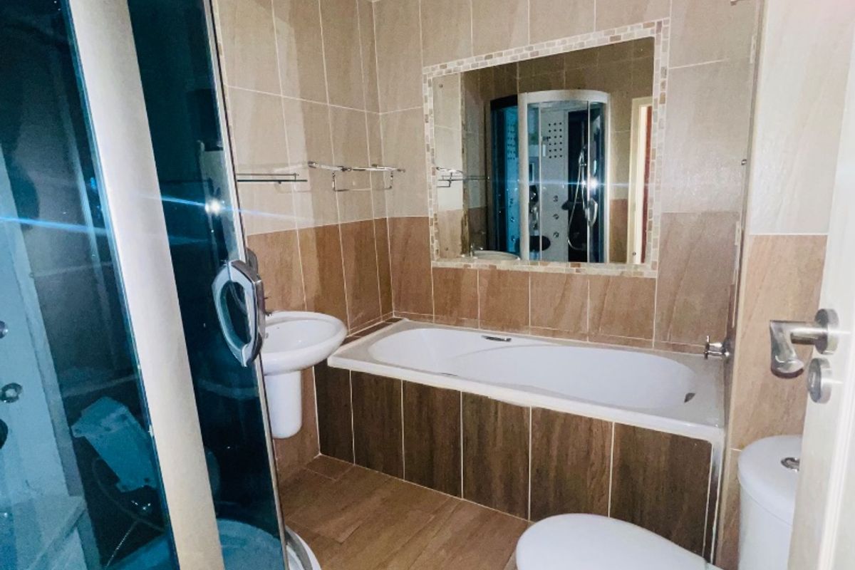 A functional bathroom featuring a separate shower enclosure, bathtub, pedestal basin, and toilet with neutral wall and floor tiling.