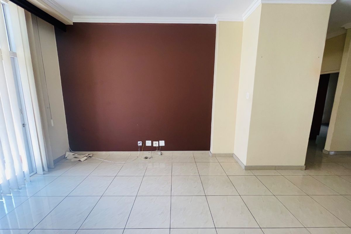 An empty living room featuring light-colored tiled flooring, crown molding, and a large sliding glass door providing natural light.